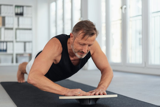 Middle-aged man exercising plank on balance board