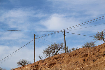 Power supply line against blue sky over arid land with leafless shrubs (Tenerife, Spain)