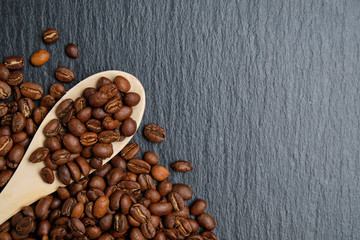 A wooden spoon with coffee beans on a slate board. Copy space. Top view.