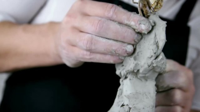 Sculptor creates a bust and puts his hands clay on the skeleton of the sculpture. Close-up