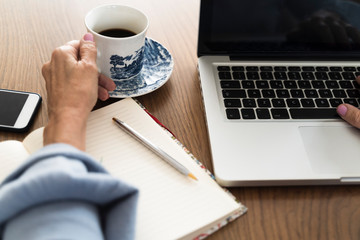 Adult woman holding a cup of coffee working on a laptop