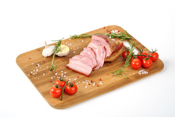 Cooked smoked meat lies on a cutting wooden board on a white background. Decorated with herbs and vegetables.
