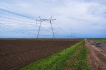 Rural landscape. Electric power lines in the field with bad road on blue sky background