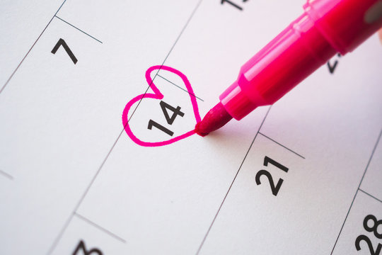 Female Hand with pen mark heart shape on calendar date at 14th valentine day