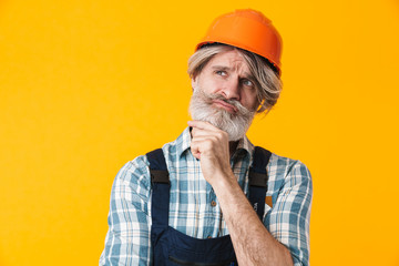 Thinking elderly grey-haired man builder in helmet