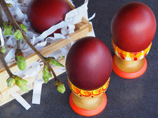 Natural Easter eggs in wooden stands and twigs with young lilac leaves on a gray background closeup. Spring bright picture with painted eggs and greenery for the Easter holiday top view.