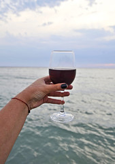 Wine glasses with red wine in female hand on the sunset beach.  