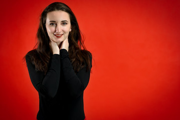 Fototapeta premium Photo of a pretty young brunette woman with a smile with good makeup on a red background. Concept girl talking in front of the camera with emotions.