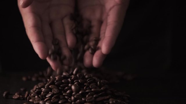 slow motion of hands pouring coffee beans to a pile of coffee beans.