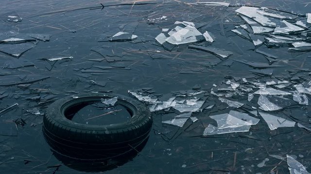  Old car tire in the water, causing environment pollution. Ice drift on the river. 