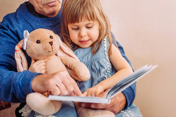 Beautiful little girl reading book with her grandfather