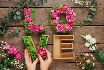 Female hands making volume letters LOVE with stabilized moss and roses on wooden background