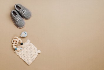 Baby wooden teether, knitted hat and shoes on beige background