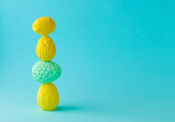 Yellow geometric Easter eggs standing on top of each other on blue background with copy space