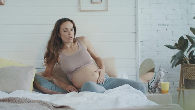 Pregnant woman surprising baby kick her belly in bed. Belly mother holding tummy