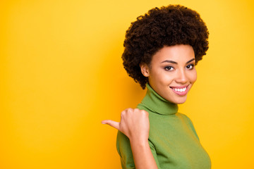 Close up turned photo of curly wavy charming woman pointing into empty space behind her back with thumb isolated vivid color background