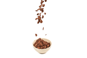 Chocolate corn flakes falling to the white bowl isolated on white. Motion.