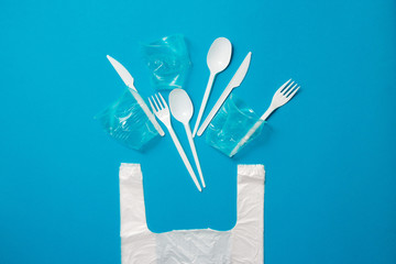 White single-use plastic knives, spoons, forks and bag on a blue background. Say no to single use...