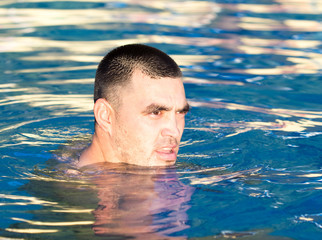 Young wet sexy muscular man posing in the swimming pool