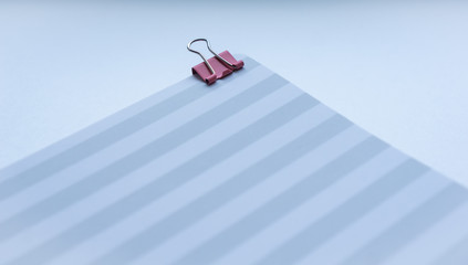 Close up of striped grey and white notebook with pink clips on top right corner on white background. Concept of education, business, minimalism. Selective focus.