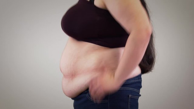 Close-up of fat unrecognizable Caucasian woman retracting belly and relaxing. Side view of obese woman's body. Obesity, overweight problem.