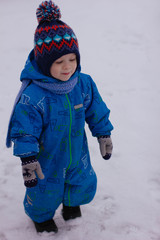Fototapeta na wymiar little boy in blue overalls in winter, it is snowing. portrait