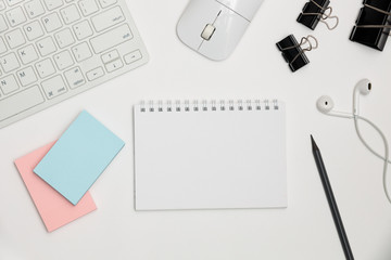 White office desk with keyboard, mouse, supplies and notepad from above. 