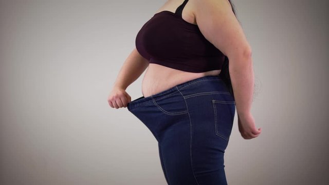 Side view of plump Caucasian woman showing stretchable jeans. Fat young unrecognizable girl getting dressed indoors. Overweight, obesity, cellulite.