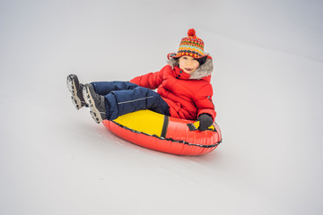 Fototapeta na wymiar Child having fun on snow tube. Boy is riding a tubing. Winter fun for children