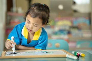 Cute little girl drawing on white board at table.