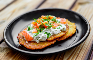potato pancakes withsalmon fish and sour cream in a plate on wooden table