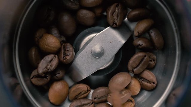 Fresh roasted coffee beans pouring in a grinder from glass jar. Barista man preparing to grind coffee, making freshly ground coffee in electric coffee mill. Top view. Slow motion.