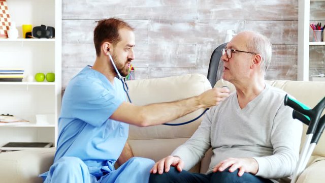 Revealing shot of young male nurse listening to old retired man heartbeat