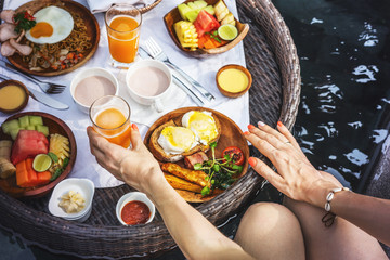 Breakfast in a wicker tray right on the water surface of the pool. Beautiful cozy luxury breakfast for two at the private pool,Bali,Indonesia. Very nice traditional breakfast in luxury hotel in Bali