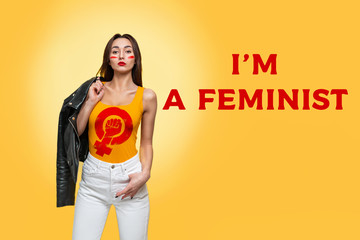 Feminism and the concept of equal rights. Caucasian young woman with a leather jacket in her hands poses confidently on a yellow background. I'm feminist and sign of girlpower