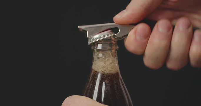 Soda glass bottle being opened by opener. Man's hands open fizzing refreshing soda aerated beverage spraying with foam flow