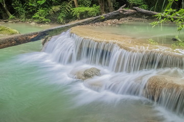 Beautiful silky water cascade flowing on cliff rocks around with blue-green water and green forest background, Erawan Waterfalls, 1th step, Kanchanaburi, west of Thailand.