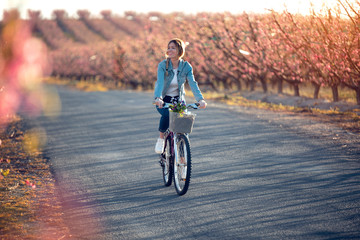 Pretty young woman riding with a bike in cherry field in springtime.