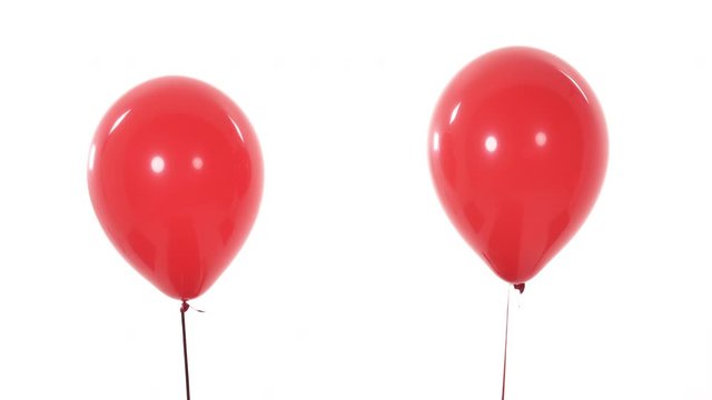 Close-up studio shot of two red balloons fly in the air and separating from each other. Isolated, on white background.