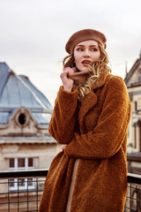 Outdoor fashion portrait of young attractive elegant woman wearing trendy brown faux fur coat, beige beret, posing in European city