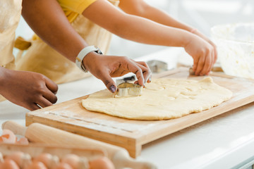 cropped view of african american mother holding cookie cutter near dough and kid in kitchen