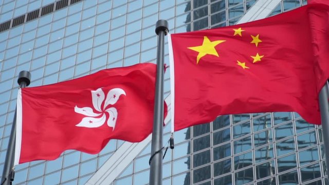Asian financial growth concept Hong Kong Flag Waving Next to China Flag with Modern Office Building in the Background Slow Motion