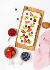 Delicious strawberry, kiwi, blueberry, raspberry cake and flowers on light gray background. Homemade summer dessert.