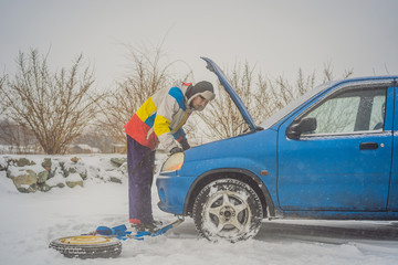 upset young men looking under the hood broken car on winter road