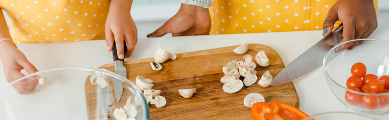 panoramic shot of african american mother and daughter holding knifes near mushrooms
