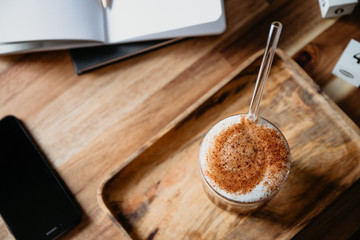 Cup of latte served with glass tube on a wooden  work desk. Coffee break concept.