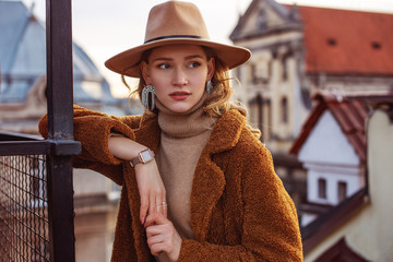 Outdoor fashion portrait of elegant woman wearing beige hat, wrist watch, turtleneck, brown faux...