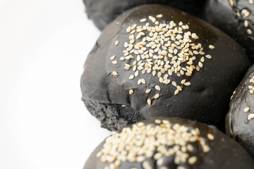 Loaf of charcoal bread bun with white sesame on top in the white plate isolated on black background