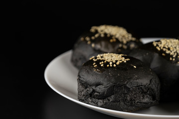 Loaf of charcoal bread bun with white sesame on top in the white plate isolated on black background