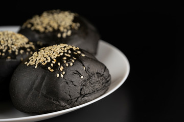 Loaf of charcoal bread bun with white sesame on top in the white plate isolated on black background